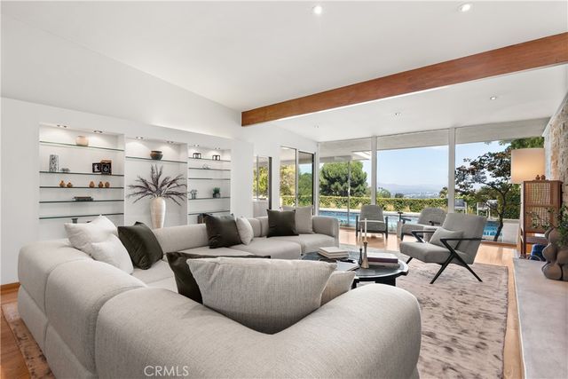 a living room with furniture large windows and a view of kitchen