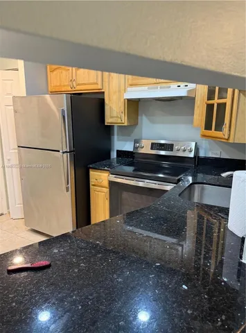 a kitchen with stainless steel appliances granite countertop a refrigerator a stove and a sink with wooden cabinets