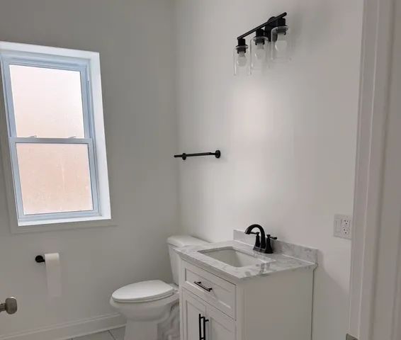 a bathroom with a granite countertop sink toilet and a window