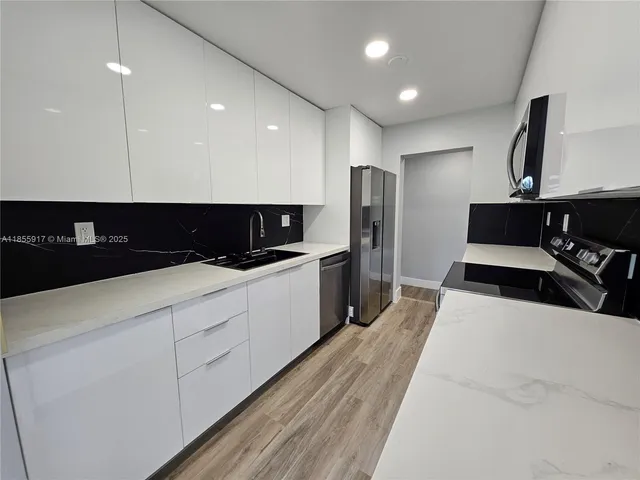 a large white kitchen with stainless steel appliances a large counter top a stove a sink a refrigerator and a cabinets