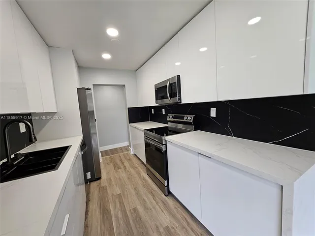 a kitchen with a sink a refrigerator and a stove top oven with wooden floor