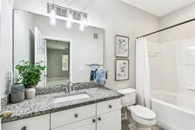 a bathroom with a granite countertop sink a toilet a mirror a vanity and shower