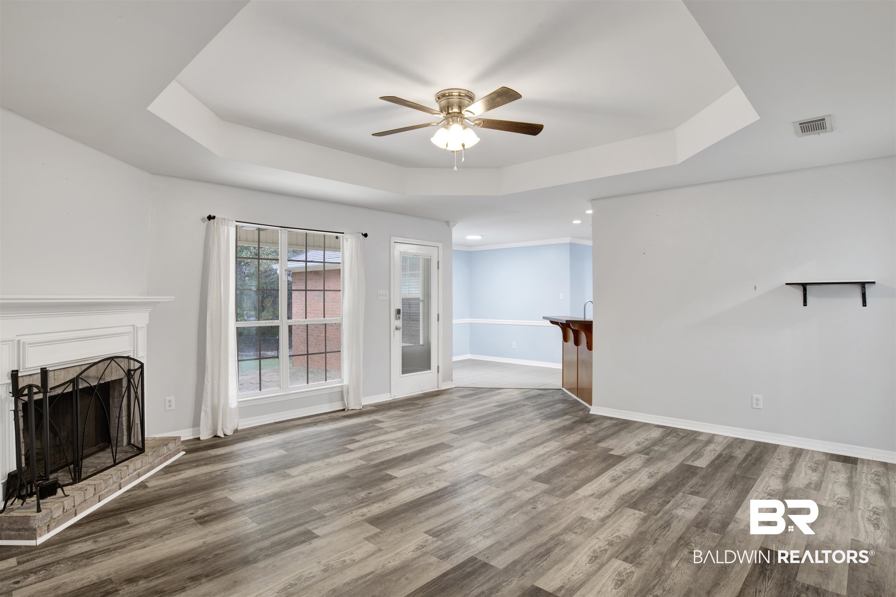 9534 Labrador Run North Mobile, AL 36695 - Photo 12 of 30 Unfurnished living room with a tray ceiling, light wood-style floors, a brick fireplace, and a ceiling fan