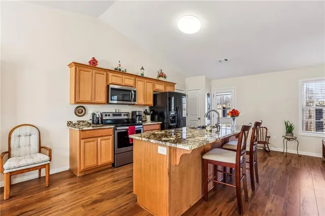 a kitchen with stainless steel appliances granite countertop a stove top oven a sink dishwasher a dining table and chairs with wooden floor