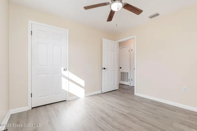 an empty room with wooden floor chandelier fan and windows