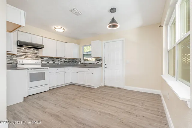 a large kitchen with stainless steel appliances granite countertop a stove a sink and white cabinets with wooden floor