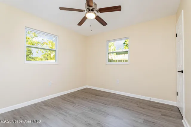 an empty room with wooden floor ceiling fan and windows