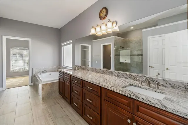 a spacious bathroom with a granite countertop double vanity sink a mirror and a bathtub