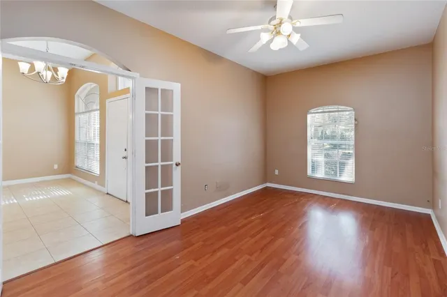 an empty room with wooden floor chandelier fan and windows