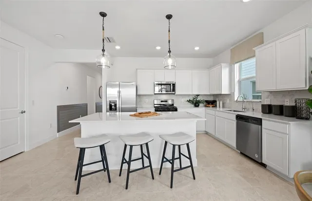 a kitchen with stainless steel appliances kitchen island granite countertop a dining table chairs and white cabinets