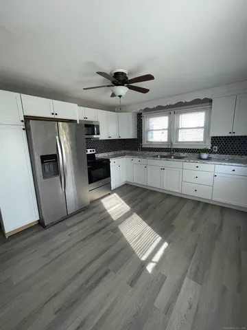 a open kitchen with stainless steel appliances granite countertop a refrigerator a sink dishwasher a stove and white countertops with wooden floor