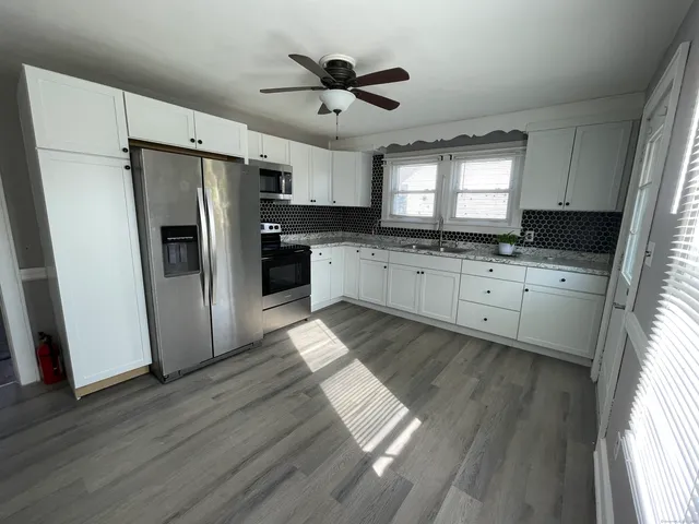 a kitchen with granite countertop a refrigerator a sink dishwasher a stove and white cabinets with wooden floor