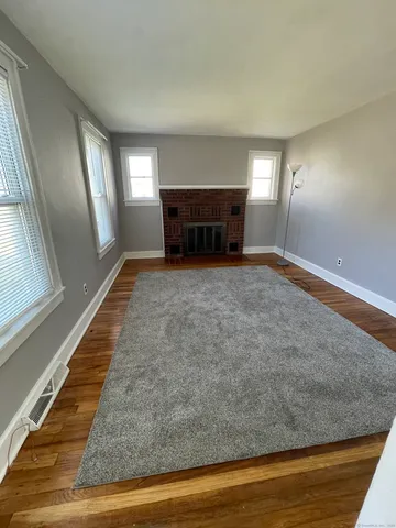 a view of an empty room with wooden floor fireplace and a window