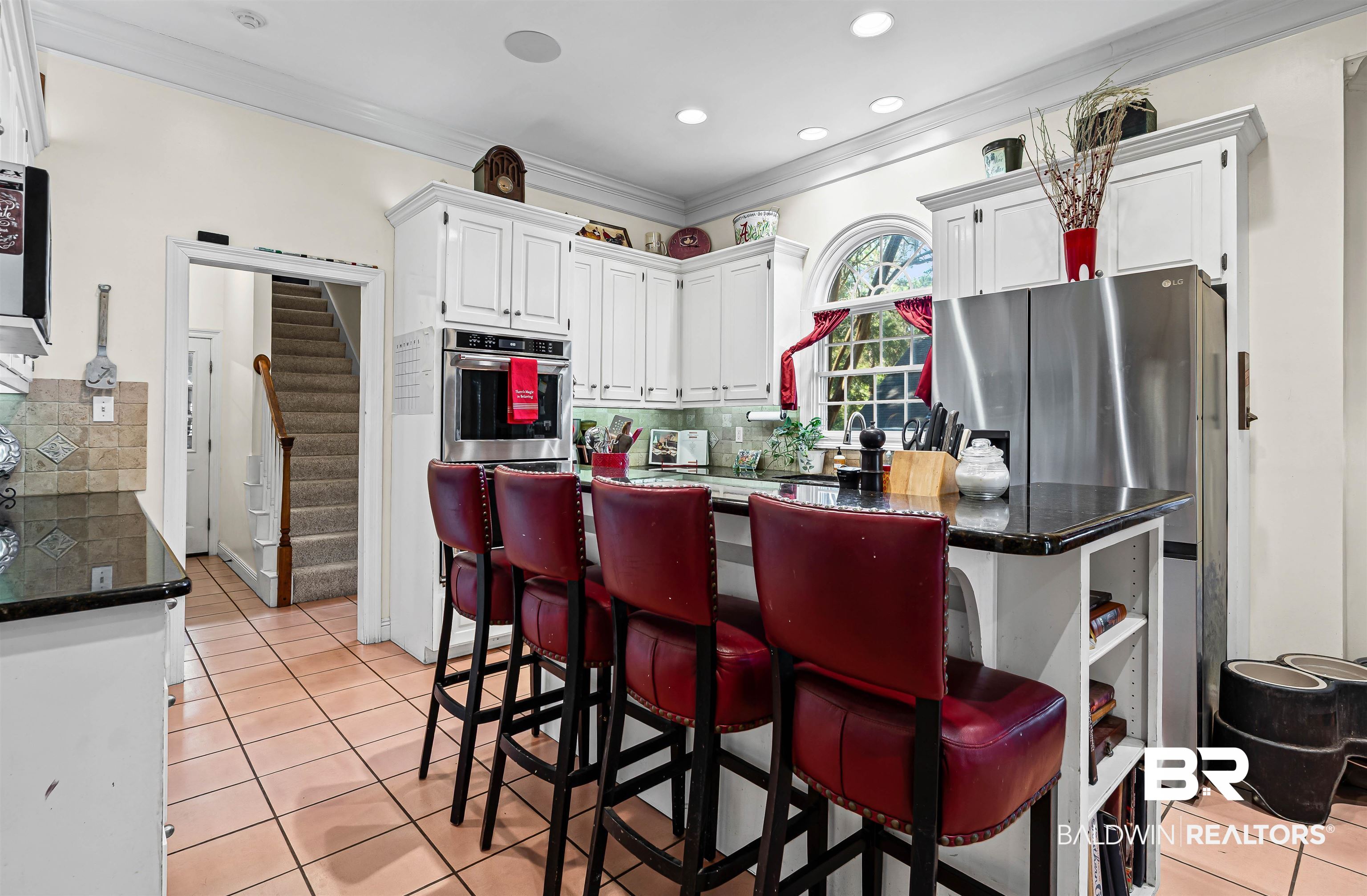 107 Beaver Dam Road Fairhope, AL 36532 - Photo 17 of 45 Kitchen with light tile patterned floors, white cabinets, a kitchen breakfast bar, crown molding, and stainless steel appliances