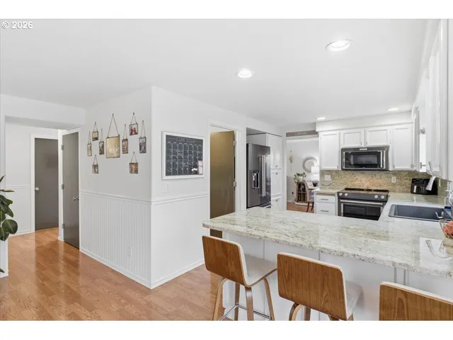 a kitchen with stainless steel appliances kitchen island granite countertop a refrigerator a stove a sink a oven with white cabinets and wooden floor