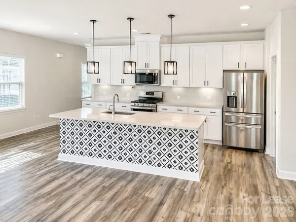 a kitchen with stainless steel appliances kitchen island granite countertop a refrigerator a sink a stove and white cabinets with wooden floor