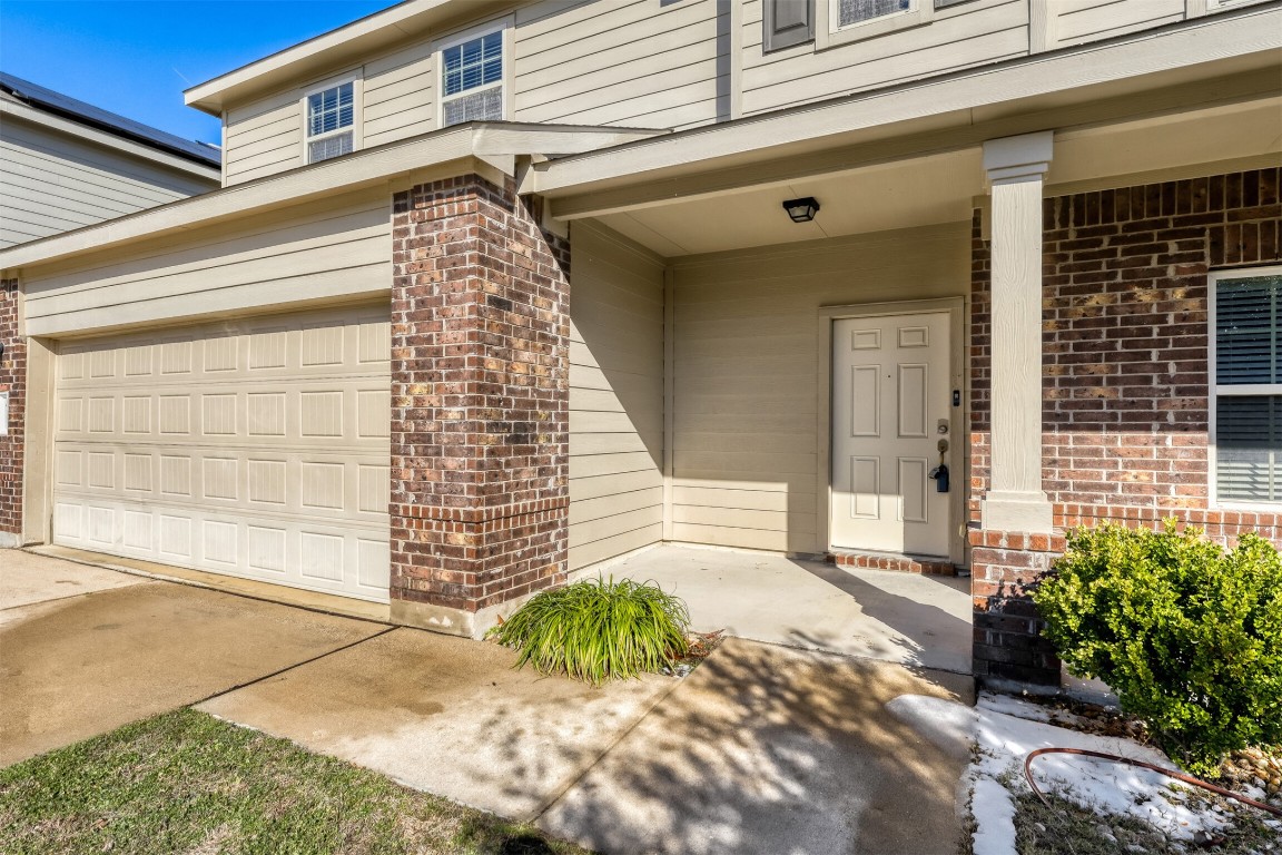 Doorway to property featuring covered porch, brick siding, and concrete driveway