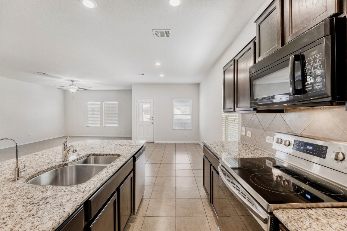 433 Druse Lane Jarrell, TX 76537 - Photo 11 of 28 Kitchen with appliances with stainless steel finishes, recessed lighting, dark brown cabinetry, light tile patterned floors, and light stone counters