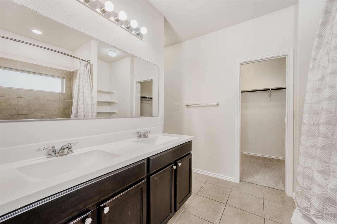 433 Druse Lane Jarrell, TX 76537 - Photo 16 of 28 Bathroom featuring a walk in closet, double vanity, a shower with shower curtain, and light tile patterned floors