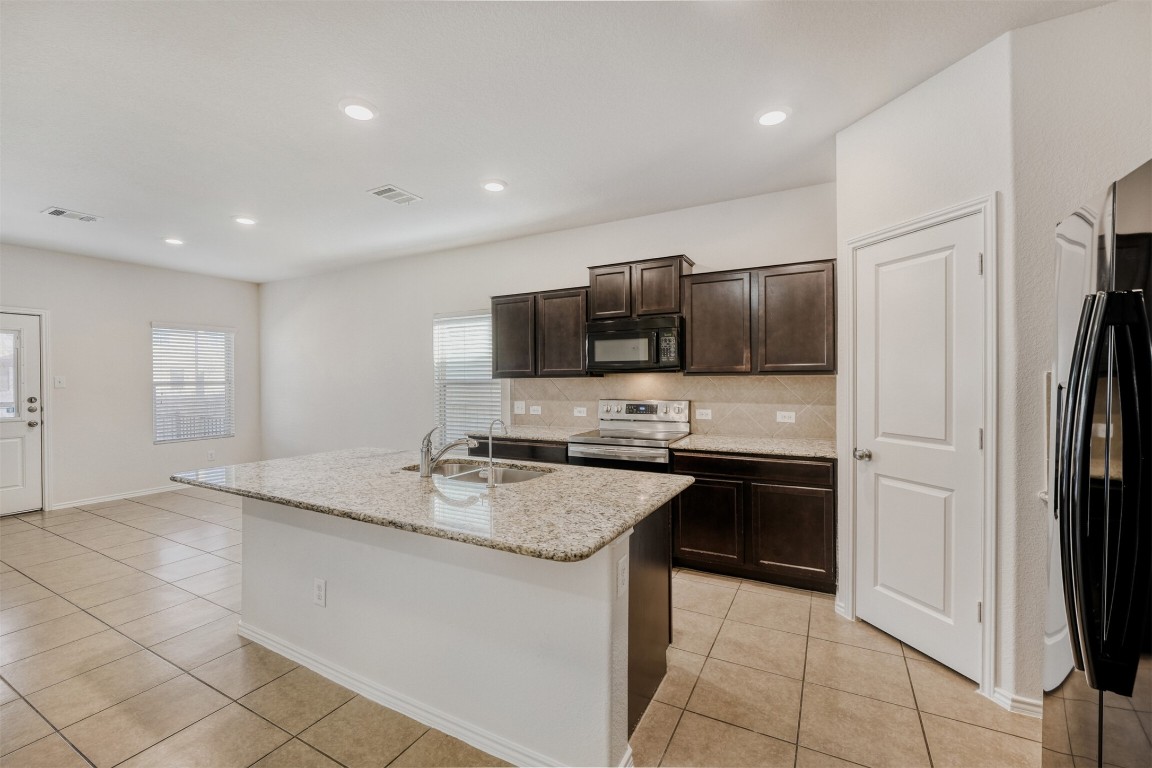 433 Druse Lane Jarrell, TX 76537 - Photo 8 of 28 Kitchen featuring stainless steel electric range oven, an island with sink, dark brown cabinetry, light stone counters, and black microwave