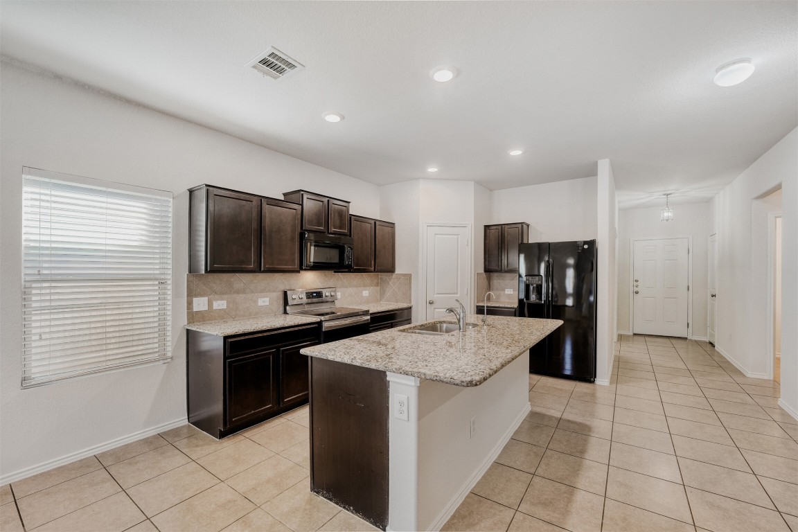 433 Druse Lane Jarrell, TX 76537 - Photo 9 of 28 Kitchen featuring dark brown cabinetry, light tile patterned floors, black appliances, tasteful backsplash, and an island with sink