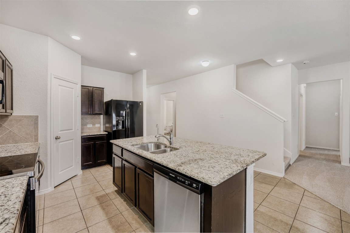 433 Druse Lane Jarrell, TX 76537 - Photo 10 of 28 Kitchen with stainless steel appliances, dark brown cabinetry, an island with sink, light tile patterned floors, and light stone countertops