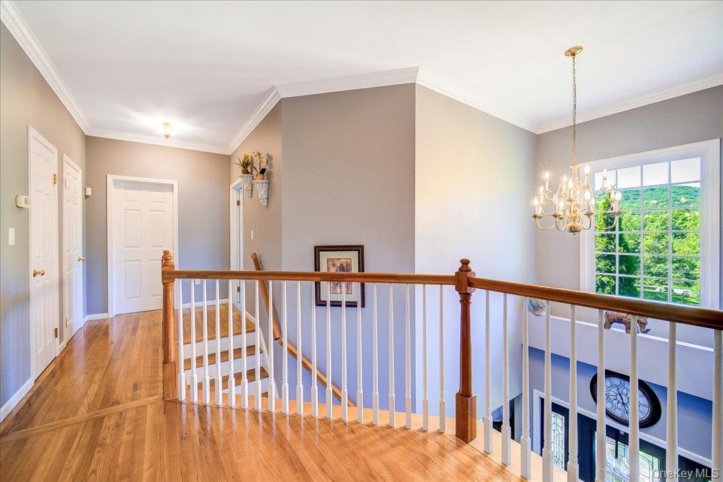 104 Wiccopee Road Putnam Valley, NY 10579 - Photo 20 of 50 Upper-level hallway featuring wood-finish flooring, white crown molding, and a traditional chandelier