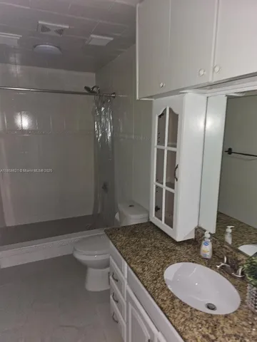 a bathroom with a granite countertop sink a toilet a mirror and shower
