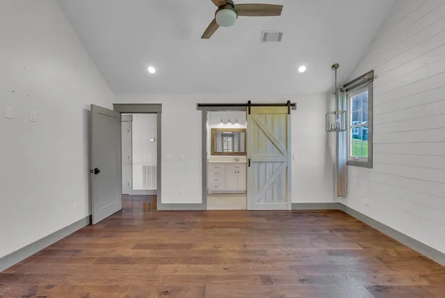 a view of an empty room with wooden floor and a ceiling fan