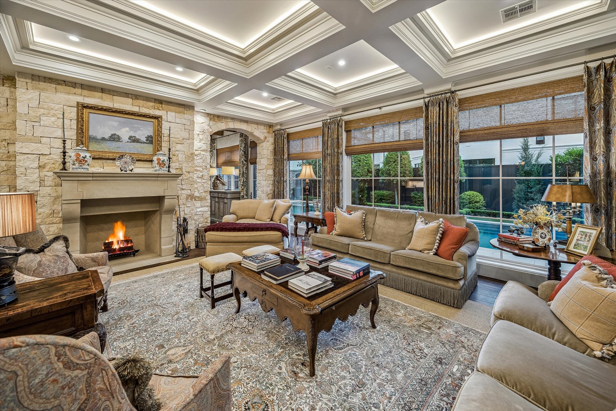 2158 Chilton Road Houston, TX 77019 - Photo 14 of 50 The family room is a warm and inviting centerpiece, featuring a box-beam coffered ceiling, designer wallpaper, and a cast stone fireplace with limestone surround. A wall of windows frames serene pool views and fills the space with natural light.