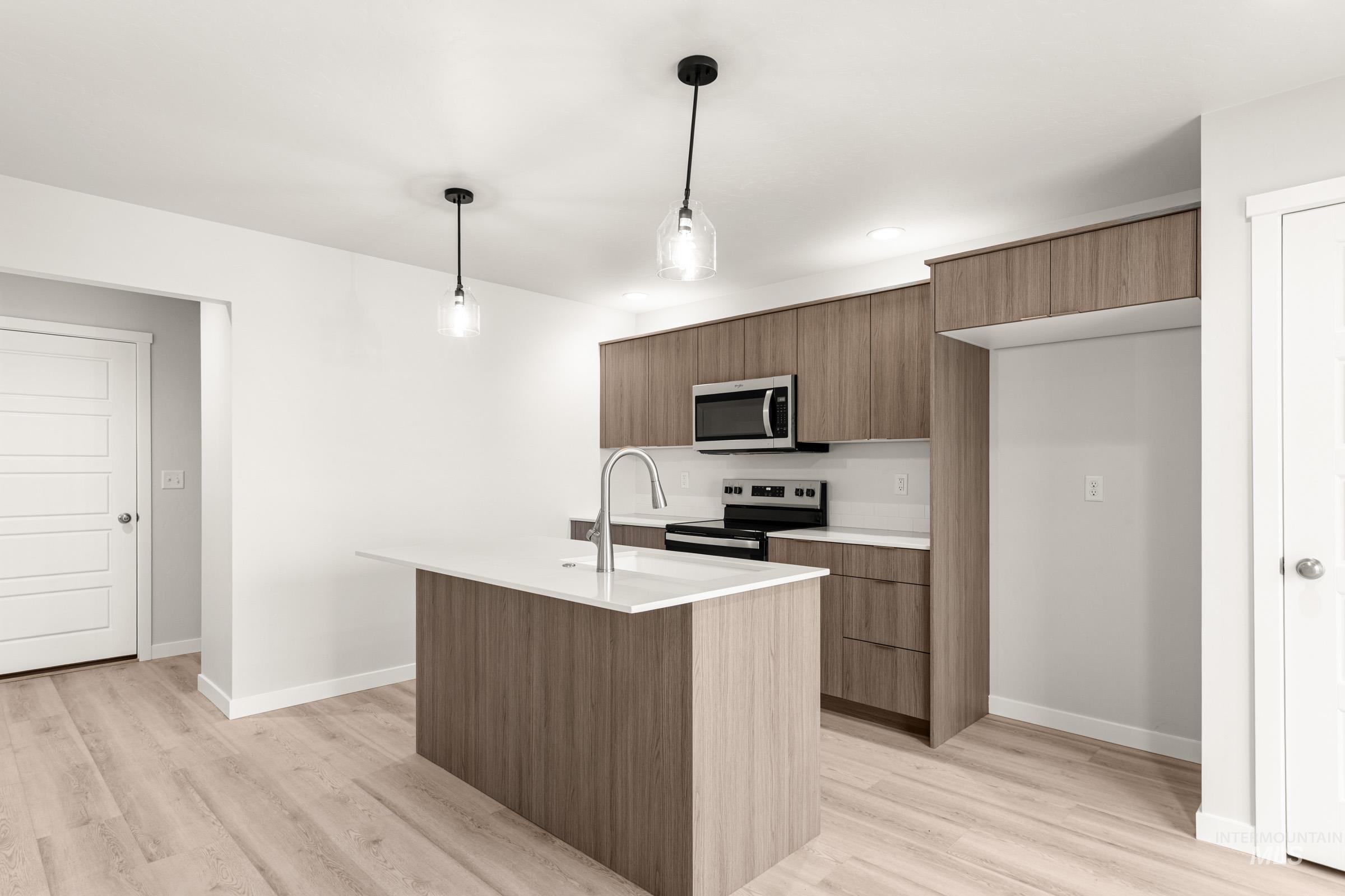 10830 Rutland Street Caldwell, ID 83605 - Photo 4 of 21 Kitchen featuring modern cabinets, stainless steel appliances, decorative light fixtures, a center island with sink, and light wood-style flooring