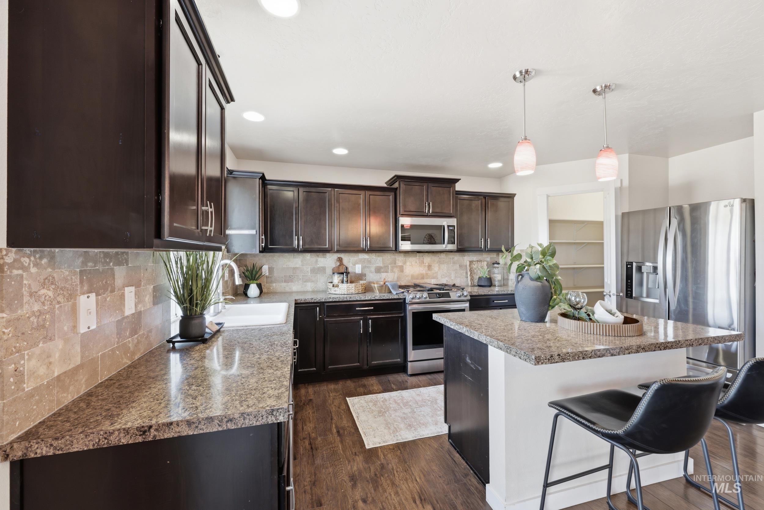 4855 South Chex Way Boise, ID 83709 - Photo 14 of 47 Kitchen featuring dark wood cabinetry, stainless steel appliances, speckled countertops, and a tile backsplash