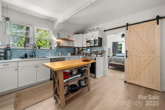 a kitchen with stainless steel appliances a stove a sink dishwasher a refrigerator white cabinets and wooden floor