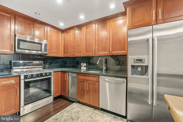 a kitchen with stainless steel appliances granite countertop a refrigerator a stove a sink and dishwasher with wooden cabinets