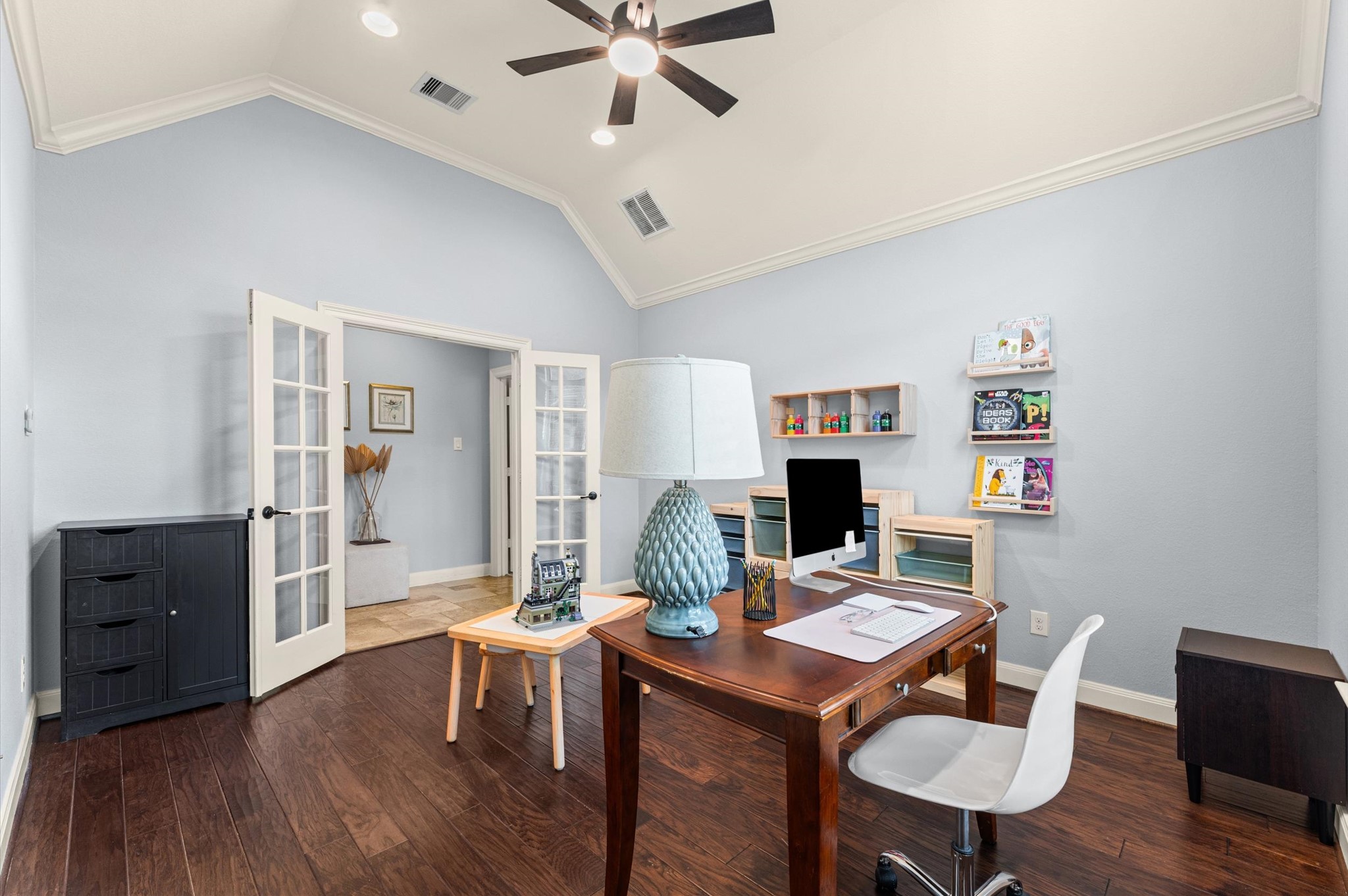 70 Valera Ridge Drive Spring, TX 77389 - Photo 26 of 37 This photo showcases a bright home office with a vaulted ceiling and recessed lighting. It features a wooden desk, modern chair, and ample storage with built-in shelves. French doors open to an adjacent room, enhancing the space with natural light and an airy feel.