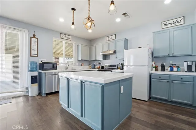 a kitchen with granite countertop a refrigerator a sink dishwasher a stove and white countertops with wooden floor