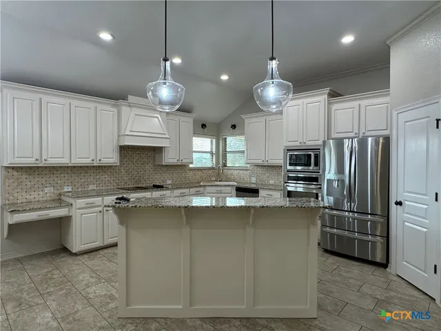 a kitchen with stainless steel appliances granite countertop a sink a stove a refrigerator cabinets and chairs