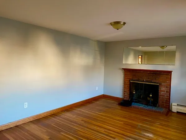 a view of an empty room with wooden floor and a fireplace