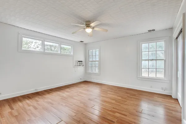 an empty room with wooden floor fan and windows