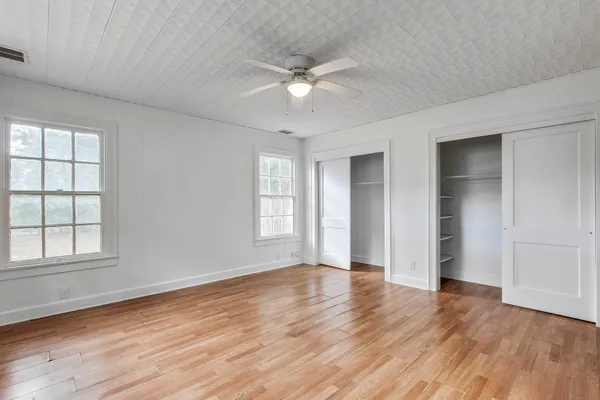 an empty room with wooden floor chandelier fan and windows