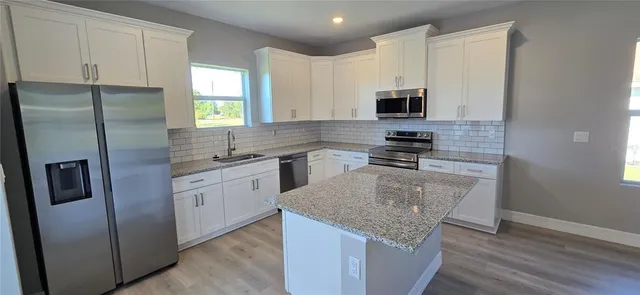 a kitchen with stainless steel appliances granite countertop a refrigerator a sink a stove a microwave and wooden floor