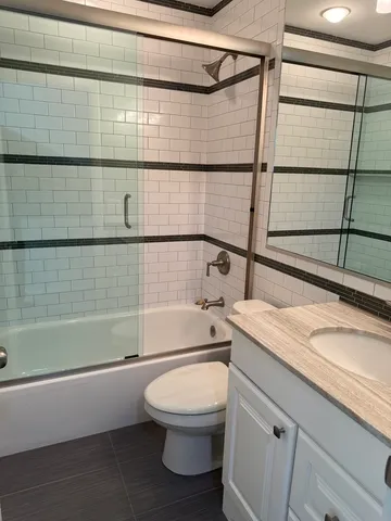 a bathroom with a granite countertop bathtub shower sink vanity and toilet