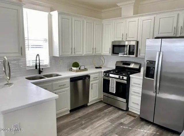 a kitchen with stainless steel appliances white cabinets a sink a stove a refrigerator and microwave