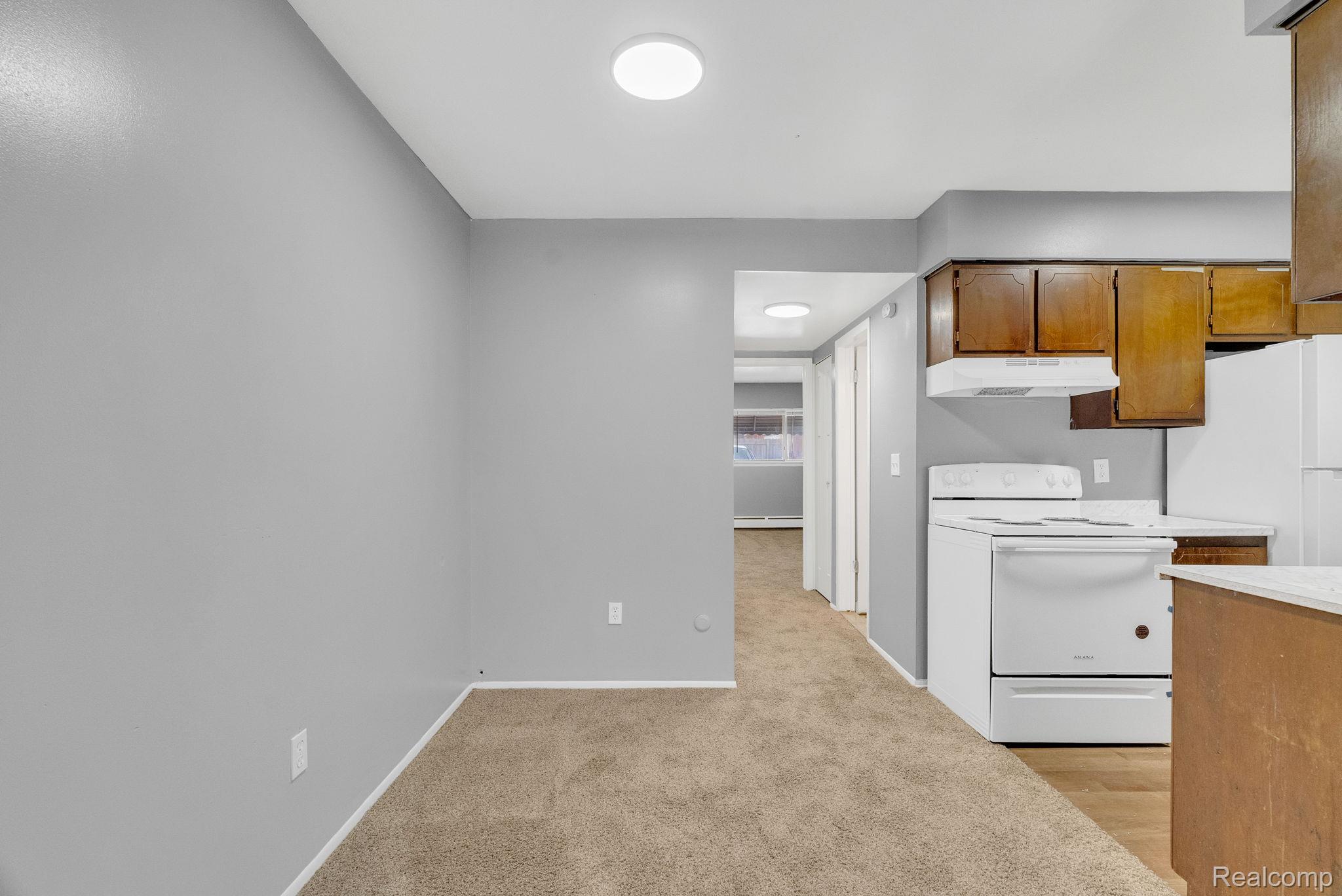 4535 Cadieux Road, Unit 42 / 210 Detroit, MI 48224 - Photo 7 of 16 Kitchen featuring white appliances, light countertops, brown cabinets, light carpet, and under cabinet range hood