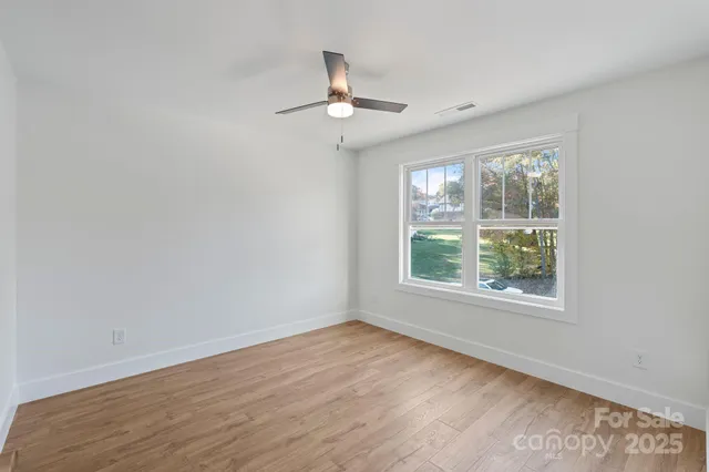an empty room with wooden floor chandelier fan and windows
