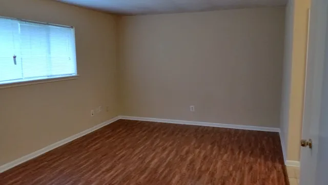 a view of an empty room with wooden floor and a window