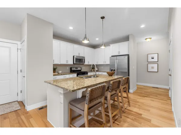 a kitchen with stainless steel appliances kitchen island granite countertop a refrigerator a stove a sink dishwasher and white cabinets with wooden floor