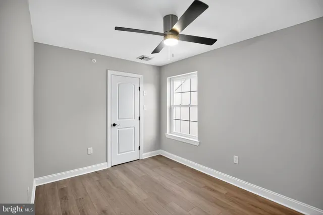 an empty room with wooden floor ceiling fan and windows