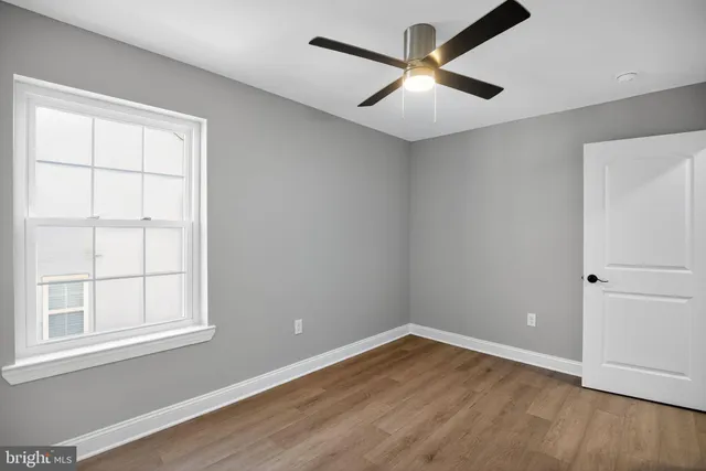an empty room with wooden floor chandelier fan and windows