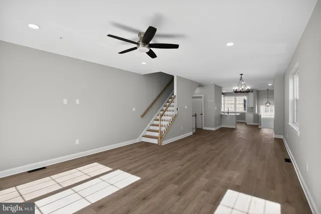 a view of an empty room with wooden floor kitchen view and a window